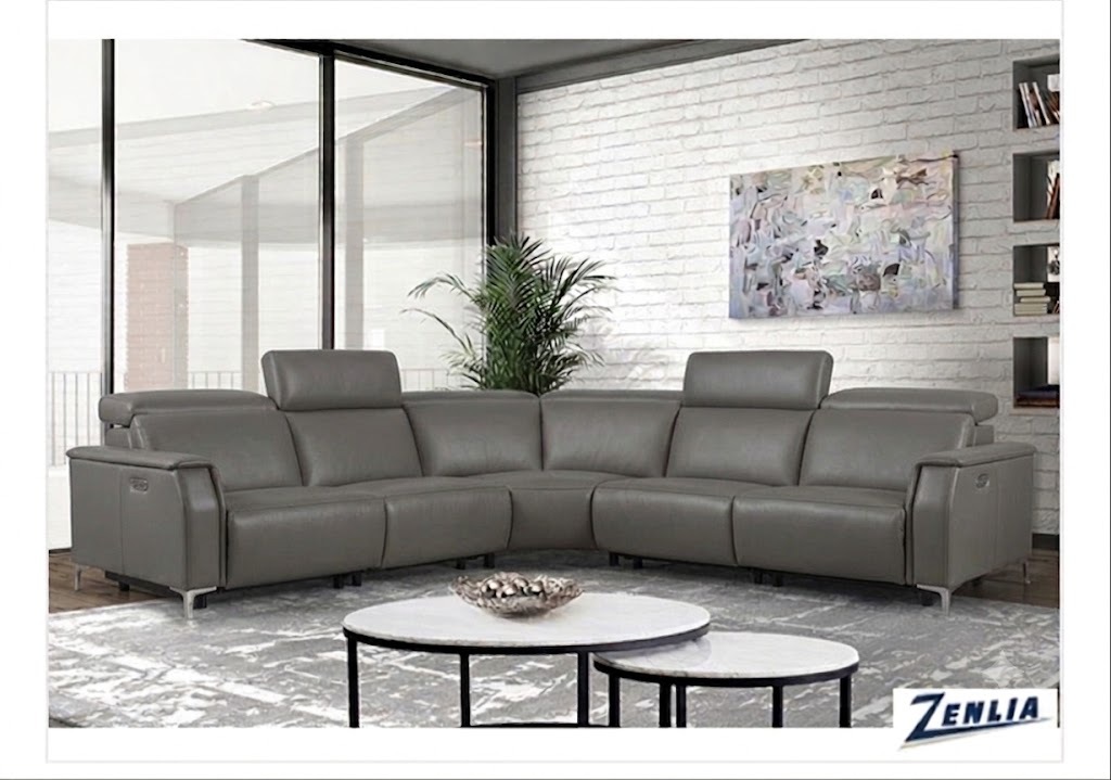 A modern living room features two sleek gray leather recliners with adjustable headrests, set against a white brick wall. A large abstract painting hangs above, and a potted plant adds a touch of greenery.